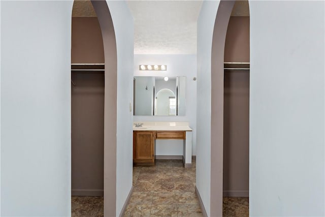 full bath with a spacious closet, a textured ceiling, vanity, and baseboards