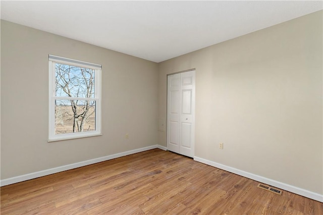 spare room featuring light wood-type flooring, visible vents, and baseboards