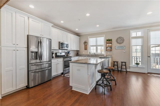 kitchen with a kitchen island, white cabinetry, stainless steel appliances, a breakfast bar area, and crown molding