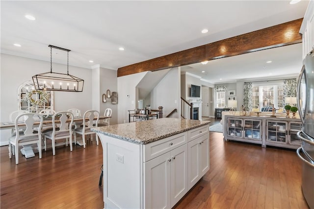 kitchen with light stone counters, dark wood-style floors, a kitchen island, white cabinets, and beamed ceiling