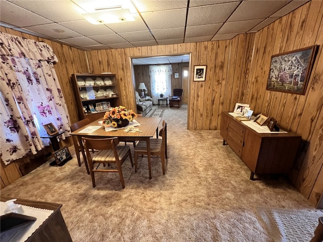 dining space featuring a paneled ceiling, light carpet, and wooden walls