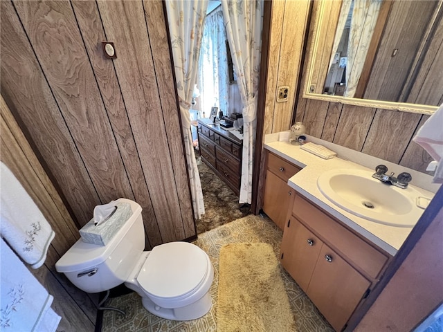 bathroom featuring toilet, wood walls, and vanity