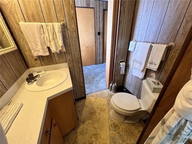 bathroom with toilet, wood walls, and vanity