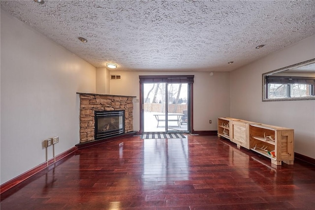 unfurnished living room featuring a stone fireplace, a textured ceiling, baseboards, and wood-type flooring