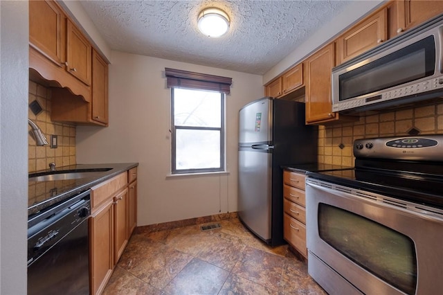 kitchen featuring a sink, brown cabinets, dark countertops, and appliances with stainless steel finishes