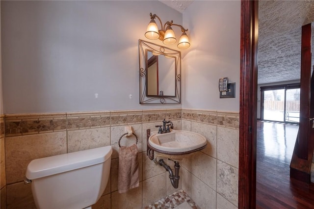 half bath with a sink, toilet, tile walls, and wainscoting