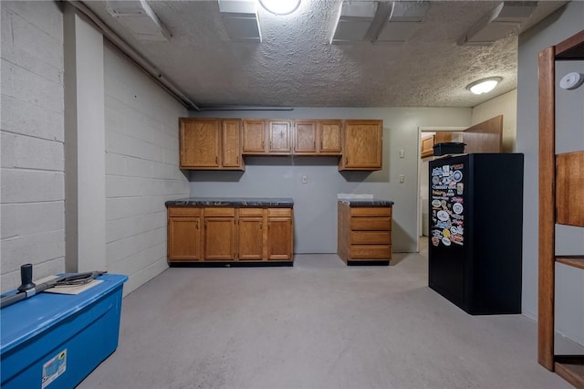 kitchen featuring concrete block wall, freestanding refrigerator, concrete flooring, a textured ceiling, and brown cabinets