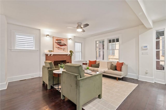 living room with dark wood-type flooring, a brick fireplace, baseboards, and ceiling fan