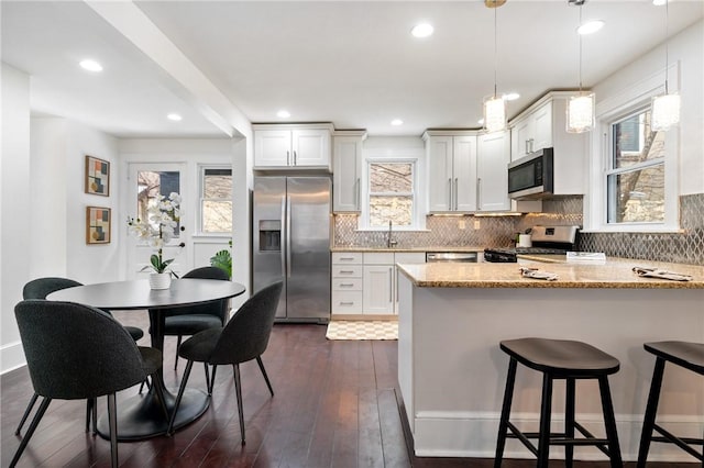 kitchen with backsplash, dark wood finished floors, stainless steel appliances, a peninsula, and light stone countertops