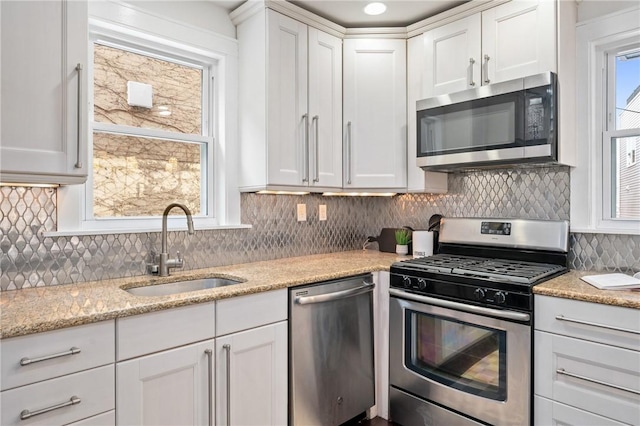 kitchen featuring light stone countertops, a sink, decorative backsplash, stainless steel appliances, and white cabinetry