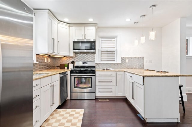 kitchen with decorative backsplash, a peninsula, stainless steel appliances, a kitchen breakfast bar, and white cabinetry