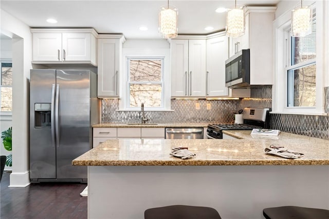 kitchen featuring light stone counters, a peninsula, white cabinets, stainless steel appliances, and a sink