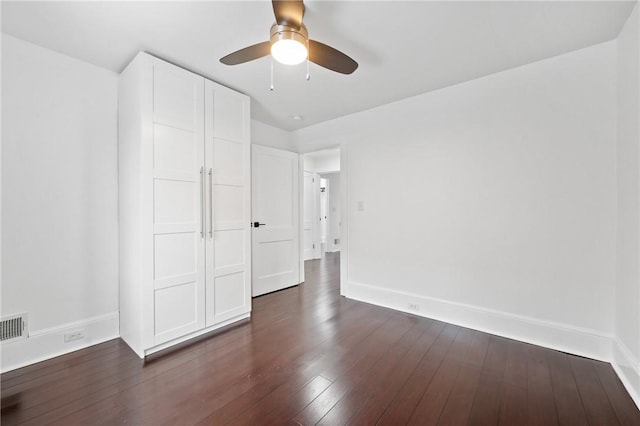 unfurnished bedroom featuring dark wood-style floors, visible vents, a ceiling fan, and baseboards