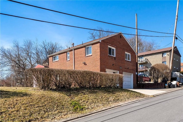 view of property exterior with concrete driveway, a garage, brick siding, and a yard