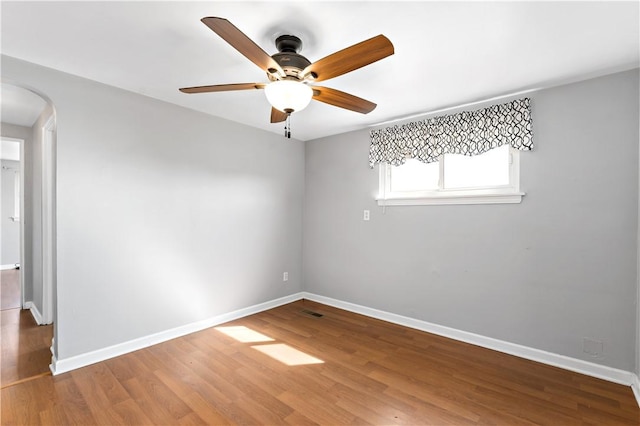 spare room featuring baseboards, arched walkways, wood finished floors, and a ceiling fan