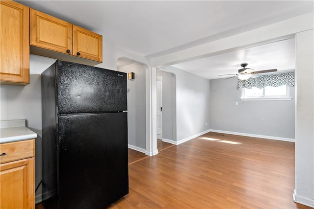 kitchen featuring a ceiling fan, freestanding refrigerator, arched walkways, light wood-style floors, and baseboards