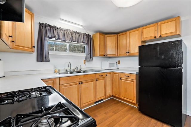 kitchen featuring black appliances, wood finished floors, light countertops, and a sink