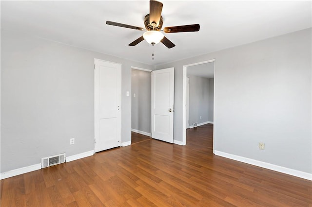 empty room with ceiling fan, wood finished floors, visible vents, and baseboards