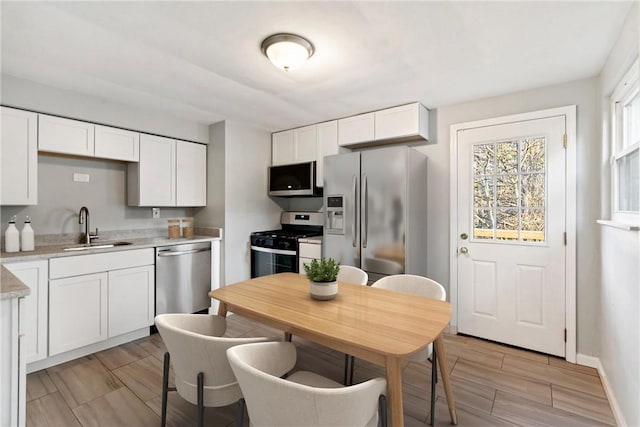 kitchen with a sink, stainless steel appliances, white cabinets, and light countertops