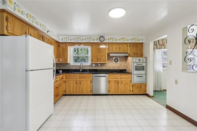 kitchen with light floors, freestanding refrigerator, a sink, under cabinet range hood, and stainless steel dishwasher