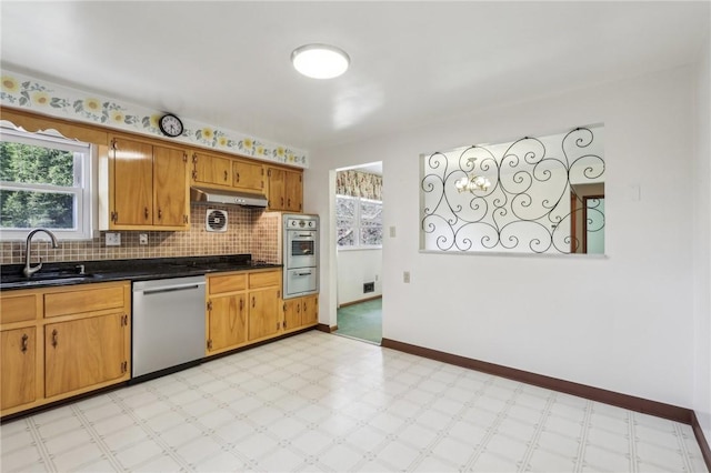 kitchen with light floors, a sink, under cabinet range hood, appliances with stainless steel finishes, and dark countertops