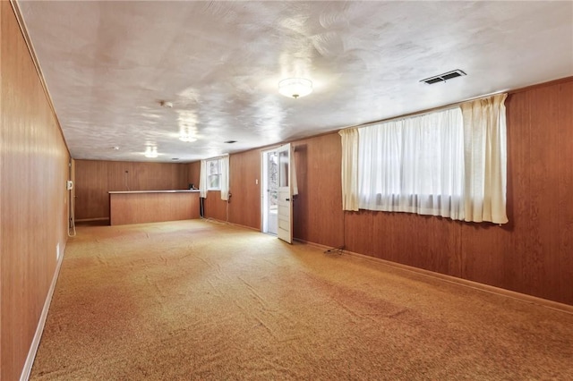 unfurnished living room with visible vents, carpet floors, baseboards, and wood walls