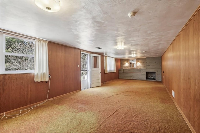 unfurnished living room with wooden walls, carpet flooring, plenty of natural light, and a large fireplace