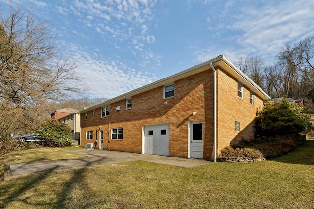 back of house featuring central air condition unit, a yard, brick siding, and driveway