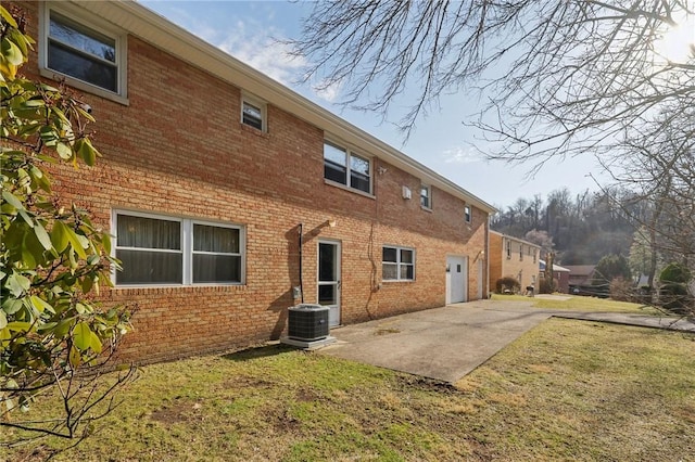 back of house featuring central AC unit, a patio area, brick siding, and a lawn