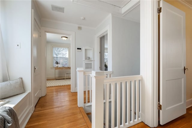 hallway with visible vents, attic access, light wood-style flooring, ornamental molding, and an upstairs landing