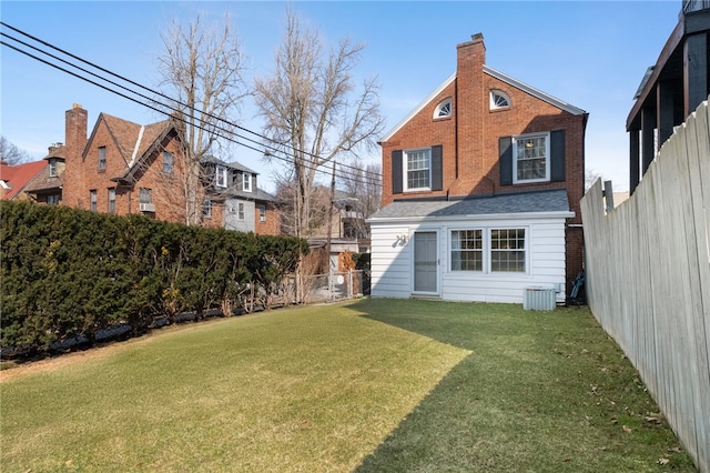 back of house featuring central AC unit, a yard, a fenced backyard, and a chimney