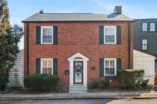 view of front of home featuring brick siding, roof with shingles, and a chimney