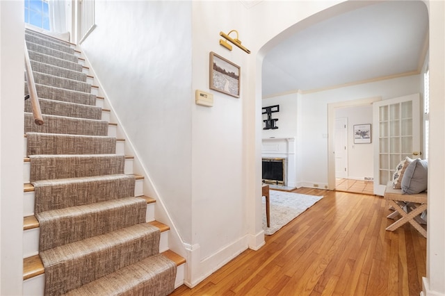 stairs featuring arched walkways, a fireplace with raised hearth, hardwood / wood-style floors, and crown molding