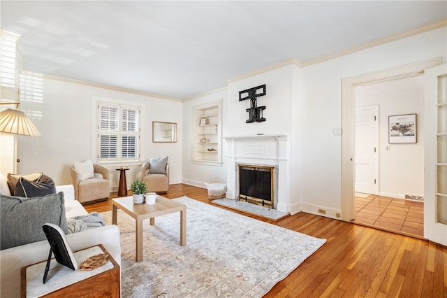 living room featuring built in features, hardwood / wood-style floors, a fireplace, and crown molding