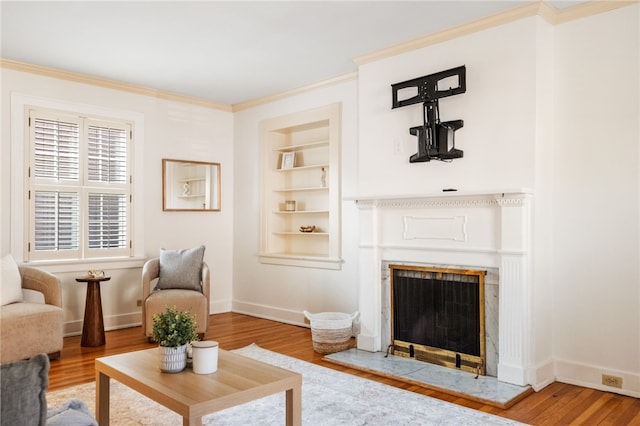 living room featuring a fireplace with raised hearth, built in features, wood finished floors, crown molding, and baseboards