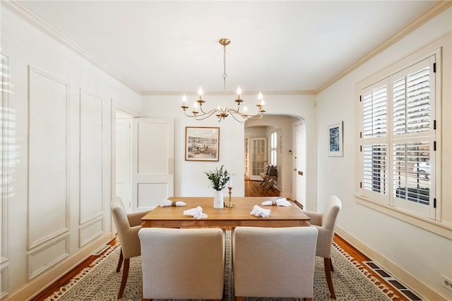 dining area with arched walkways, wood finished floors, an inviting chandelier, and ornamental molding