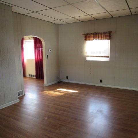 unfurnished room with visible vents, arched walkways, plenty of natural light, and wood finished floors