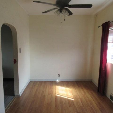 spare room with arched walkways, light wood-style flooring, baseboards, and ceiling fan