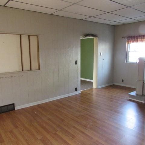 spare room with wood finished floors, visible vents, a drop ceiling, and baseboards