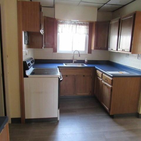 kitchen featuring dark countertops, white range with electric cooktop, a drop ceiling, light wood-type flooring, and a sink