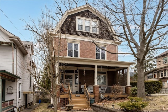 view of front facade with brick siding, a gambrel roof, and a porch