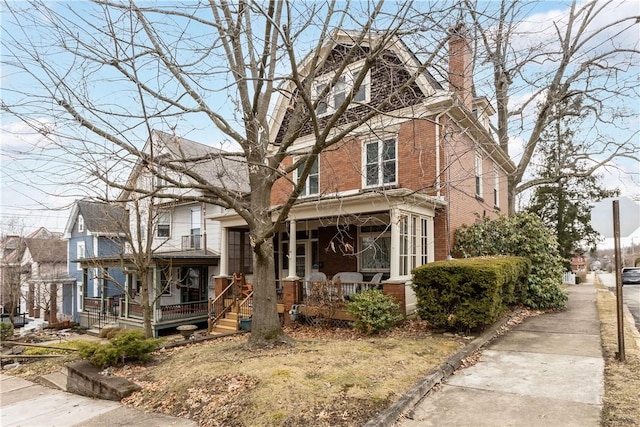 view of front of property featuring a porch, brick siding, and a chimney