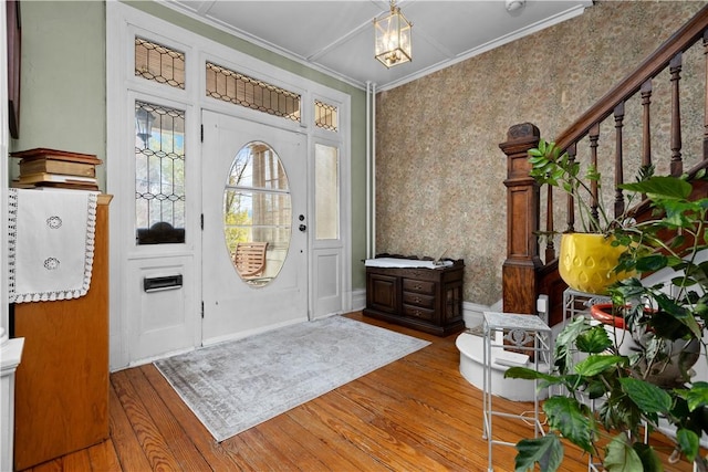 entrance foyer featuring stairway, wood finished floors, baseboards, wallpapered walls, and ornamental molding