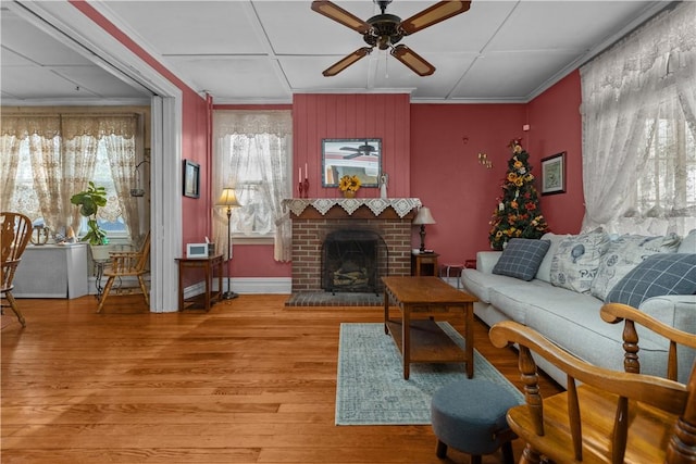 living area featuring baseboards, ceiling fan, ornamental molding, light wood-style floors, and a brick fireplace