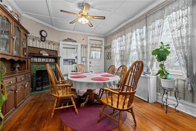 dining space with hardwood / wood-style floors, crown molding, a fireplace with flush hearth, and ceiling fan