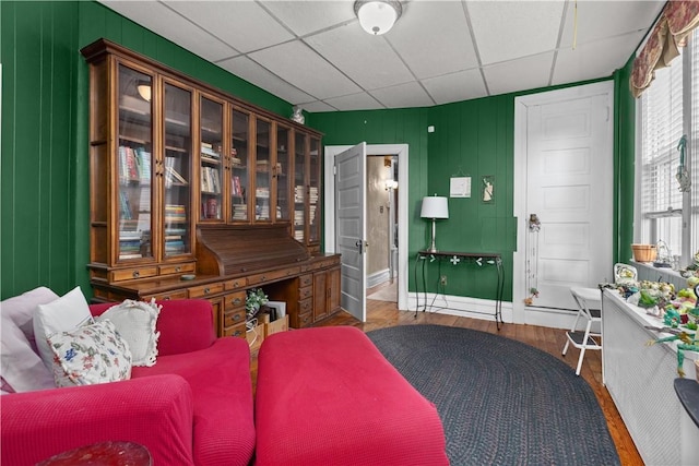 interior space featuring a paneled ceiling, baseboards, and wood finished floors