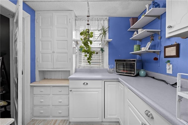 kitchen with open shelves, a textured ceiling, white cabinets, and light countertops