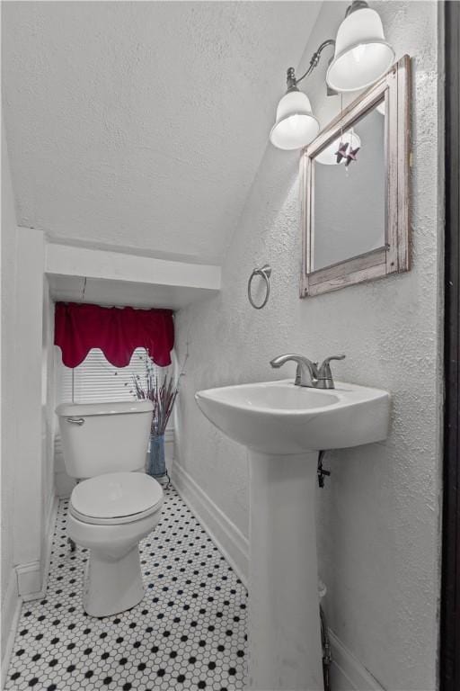 bathroom featuring baseboards, a textured ceiling, tile patterned floors, toilet, and a textured wall