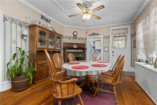 dining area featuring a brick fireplace, radiator heating unit, hardwood / wood-style floors, coffered ceiling, and a ceiling fan