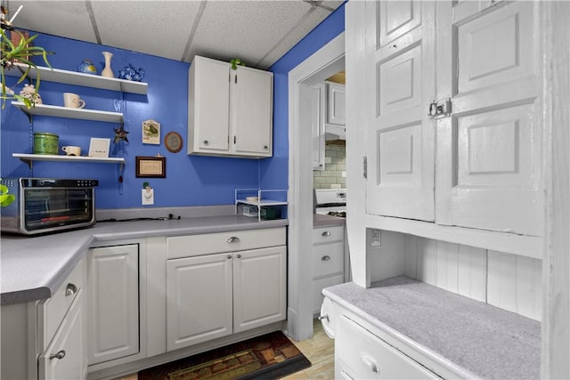 kitchen with a toaster, light countertops, white cabinets, a paneled ceiling, and under cabinet range hood